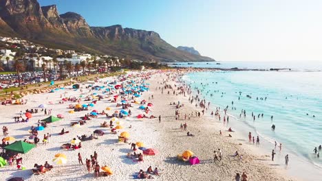 Spectacular-aerial-over-a-crowded-and-busy-holiday-beach-at-Camps-Bay-Cape-Town-South-Africa-with-Twelve-Apostles-mountains-background-2