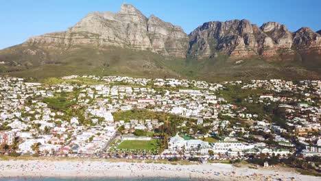 Aerial-moving-along-the-wealthy-shoreline-and-elegant-homes-of-Camps-Bay-Cape-Town-South-Africa-with-Twelve-Apostles-mountains-background