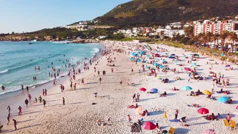 Spectacular-aerial-over-a-crowded-and-busy-holiday-beach-at-Camps-Bay-Cape-Town-South-Africa-with-Lion's-Head-mountain-background-1