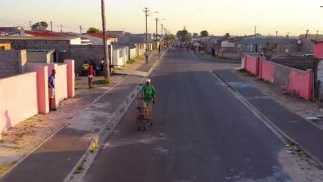 Antenne-über-Straßenszene-In-Der-Township-Von-Südafrika-Mit-Mann-Und-Einkaufswagen,-Die-Auf-Straßen-Gehen