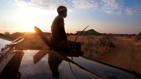 A-native-spotter-guide-sits-on-the-front-of-a-safari-jeep-vehicle-spotting-wildlife-on-the-plains-of-Africa-at-sunset-1