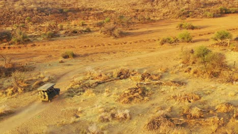 Antenne-Eines-Safari-Jeeps,-Der-Auf-Den-Ebenen-Afrikas-Im-Erindi-Wildreservat-In-Namibia-Reist,-Mit-Einheimischem-San-Tribal-Spotter-Führer,-Der-Auf-Der-Vorderseite-Sitzt-Und-Wildtiere-Beobachtet-4