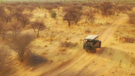 Antenne-Eines-Safari-Jeeps,-Der-Auf-Den-Ebenen-Afrikas-Im-Erindi-Wildreservat-In-Namibia-Reist,-Mit-Einheimischem-San-Tribal-Spotter-Führer,-Der-Auf-Der-Vorderseite-Sitzt-Und-Wildtiere-Beobachtet-6