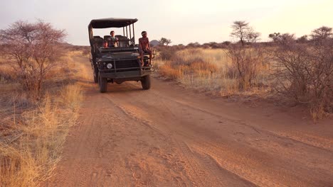 A-safari-jeep-passes-by-at-sunset-on-the-plains-of-Africa-Erindi-Park-Namibia-with-native-tribal-spotter-riding-on-front