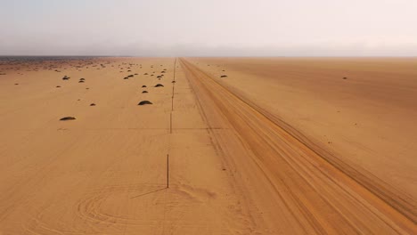 Nice-high-aerial-of-a-dirt-road-heading-across-a-flat-desert-with-mist-or-fog-in-the-distance-Namibia