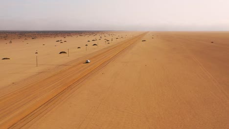 Nice-high-vista-aérea-of-a-safari-vehicle-on-a-dirt-road-heading-across-a-flat-desert-with-mist-or-fog-in-the-distance-Namibia