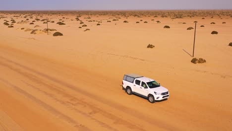 Antena-De-Un-Vehículo-De-Safari-En-Un-Camino-De-Tierra-Que-Cruza-Un-Desierto-Plano-Con-Niebla-O-Niebla-En-La-Distancia-Namibia