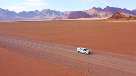 High-aerial-over-a-Toyota-safari-vehicle-heading-across-the-flat-barren-Namib-Desert-in-Namibia