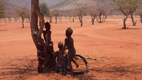 Arme-Afrikanische-Kinder-Spielen-Mit-Einem-Fahrradrad-Als-Spielzeug-In-Einem-Himba-dorf-An-Der-Grenze-Von-Namibia-Angola-1