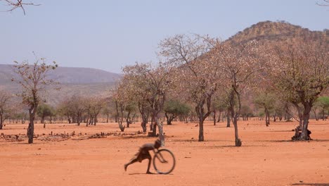 Armes-Afrikanisches-Kind-Spielt-Mit-Einem-Fahrradrad-Als-Spielzeug-In-Einem-Himba-dorf-An-Der-Grenze-Von-Namibia-Angola