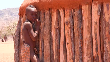 Ein-Junger-Afrikanischer-Himba-Stammesjunge-Lehnt-Sich-In-Einem-Kleinen-Dorf-In-Namibia-An-Seine-Lehm--Und-Holzhütte