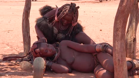 Una-Mujer-Himba-Tiene-Su-Increíble-Cabello-Trenzado-Y-Con-Rastas-Cubiertas-De-Barro-Peinado-Por-Otra-Mujer-En-Un-Pequeño-Pueblo-En-La-Frontera-De-Namibia-Y-Angola