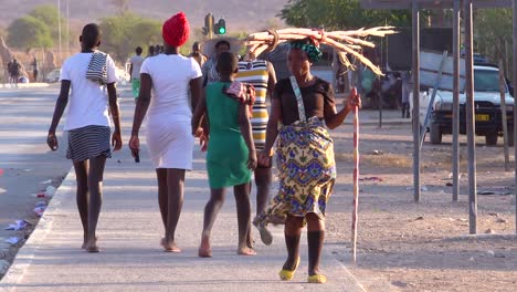 A-tribal-woman-walks-on-the-streets-of-a-market-town-in-Africa-Opuwo-Namibia-with-firewood-balanced-on-head