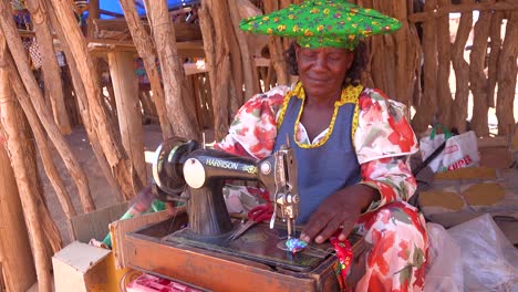 Eine-Afrikanische-Herero-Stammesfrau-In-Hellen-Modekostümen-Betreibt-Eine-Antike-Nähmaschine-Auf-Einem-Marktplatz-In-Namibia-Afrika