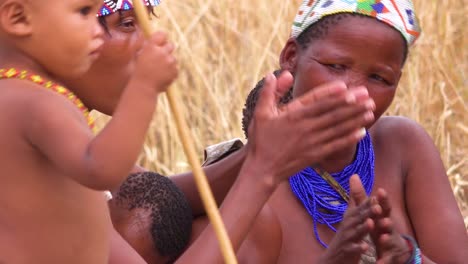 Afrikanische-San-Buschmänner-Frauen-Kinder-Und-Stammes-Eingeborene-Sitzen-In-Einem-Kreis-Singend-Und-Klatschen-In-Einem-Kleinen-Dorf-In-Namibia