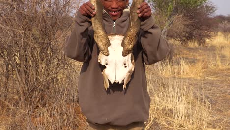 Ein-San-Buschmann-Jäger-Hebt-Einen-Tierschädel-Auf-Den-Ebenen-Afrikas-Auf