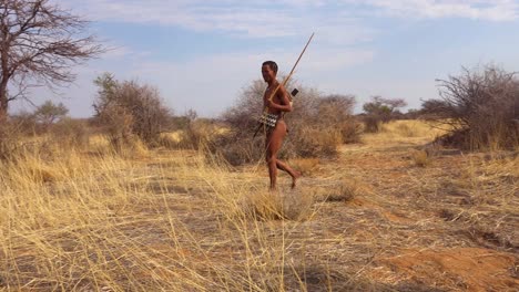A-San-bushman-hunter-walking-in-the-savannah-past-the-skull-of-an-animal-an-African-indigenous-hunter