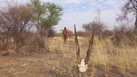 Ein-San-Buschmann-Jäger,-Der-In-Der-Savanne-Am-Schädel-Eines-Tieres-Vorbeigeht-Ein-Afrikanischer-Indigener-Jäger-1