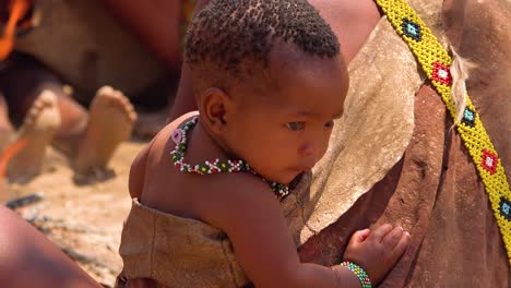Ein-Baby-Schaut-Zu,-Während-Afrikanische-San-Stammes-Buschmänner-In-Einem-Kleinen-Primitiven-Dorf-In-Namibia-Afrika-Einen-Feuertanz-Aufführen