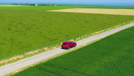 Aerial-of-a-red-car-traveling-through-green-fields-of-Normandy-France-1