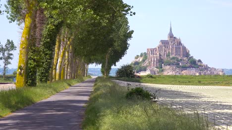 Eine-Hübsche-Straße-Durch-Die-Landschaft-Mit-Der-Klosterinsel-Mont-Saint-Michel-In-Der-Ferne-Normandie-Frankreich