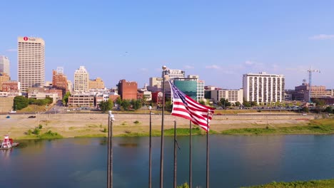 Aerial-around-flagpole-and-American-flag-with-Mississippi-River-riverboats-and-city-of-Memphis-downtown-business-district-skyline-background