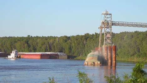 Workers-load-a-grain-barge-along-the-Mississippi-River-while-a-tugboat-arrives-nearby
