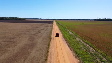 Aerial-shot-of-a-red-pickup-truck-traveling-on-a-dirt-road-in-a-rural-farm-area-of-Mississippi