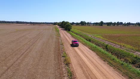Aerial-shot-of-a-red-pickup-truck-traveling-on-a-dirt-road-in-a-rural-farm-area-of-Mississippi-2