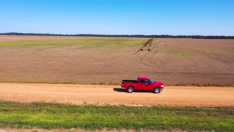 Vista-Aérea-shot-of-a-red-pickup-truck-traveling-on-a-dirt-road-in-a-rural-farm-area-of-Mississippi-4
