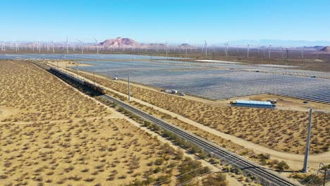 Antena-De-Drone-De-Un-Tren-De-Mercancías-Que-Viaja-A-Través-De-Una-Gran-Variedad-De-Energía-Solar-Y-Eólica-En-El-Desierto-De-Mojave,-California