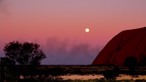 Beautiful-shot-of-the-full-moon-rising-next-to-Ayers-Rock-Uluru-Australia-during-a-dust-storm