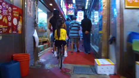 Following-shot-of-a-child-riding-on-a-bicycle-through-an-indoor-market-in-Hong-Kong