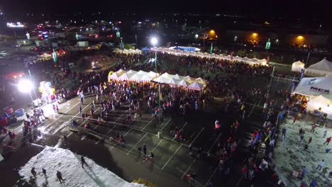 Aerial-Over-A-Carnival-Or-Fair-Held-In-A-Mall-Parking-Lot-With-Crowds-And-Booths-And-Rides
