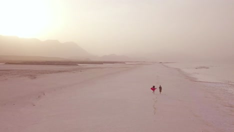 Antenne-über-Ein-Model-Veröffentlichtes-Paar,-Das-An-Einem-Breiten-Sandstrand-An-Der-Küste-Von-Dschibuti-Läuft-Und-Spaß-Hat