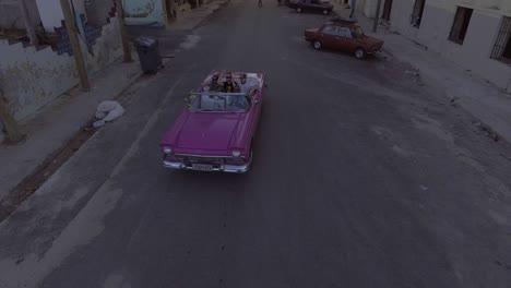 Rising-drone-aerial-of-a-group-of-tourists-riding-in-a-classic-old-car-through-the-streets-of-Havana-Cuba