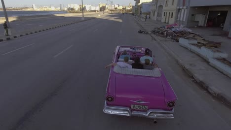 Drone-aerial-of-a-group-of-tourists-riding-in-a-classic-old-car-through-the-streets-of-Havana-Cuba-1