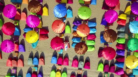 Aerial-over-a-woman-relaxing-beneath-colorful-beach-umbrellas-in-Sanur-or-Kuta-beach-on-the-coast-of-Bali-Indonesia
