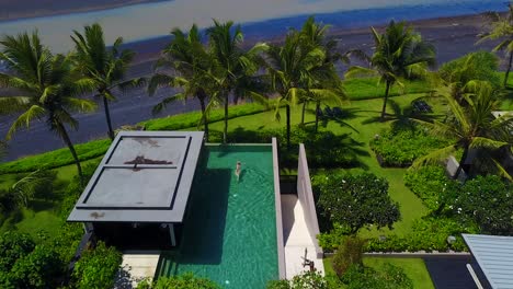 Antenne-über-Einer-Frau,-Die-In-Einem-Infinity-Pool-Im-Luxusresort-Eines-Eleganten-Wohnkomplexes-Entlang-Der-Küste-Von-Bali-Indonesien-Schwimmt?