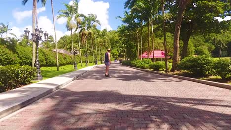 A-man-rides-a-skateboard-down-a-brick-driveway-on-a-tropical-caribbean-island