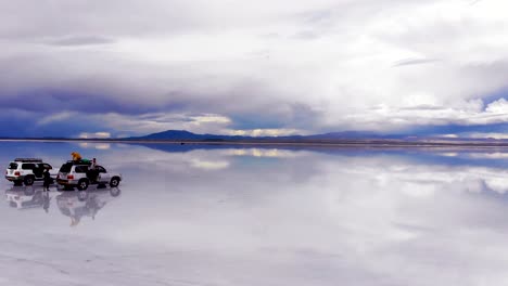 Antenne-Von-Menschen-Und-Jeeps-Auf-Dem-Uyuni-Salzsee-Mit-Perfekten-Reflexionen-In-Bolivien