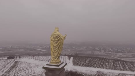 Aerial-of-golden-statue-of-Jesus-Christ-with-outstretched-arms-in-Fatima-Portugal-in-snowy-winter-weather