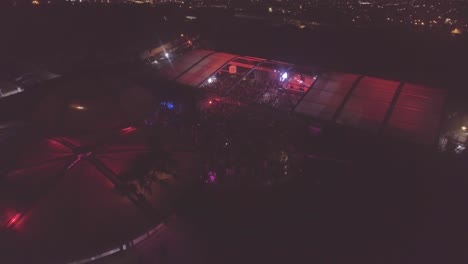 Slow-descent-aerial-over-a-massive-indoor-outdoor-rock-concert-or-dance-club-at-night-with-huge-crowds
