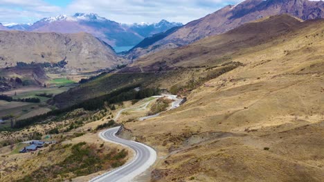 Aerial-Shot-Over-A-Road-In-The-South-Island-Of-New-Zealand-Reveals-Queenstown-And-Remarkables-Mountain-Range-Distant