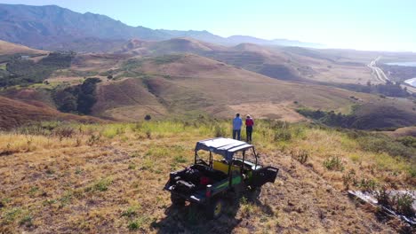 Vista-Aérea-Of-A-Senior-Retirement-Man-And-Woman-Standing-Beside-Atv-At-Magnificent-Coast-Overlook-Of-Gaviota-Coast-Pacific-Ocean-And-Santa-Barbara-County-California-1