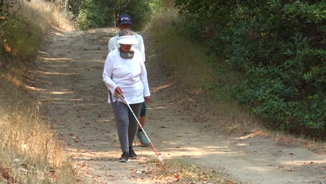 A-Blind-Woman-Walks-With-A-Cane-Through-A-Natural-Area-With-A-Guide-Helping-Her-Explore-The-Wilderness-2
