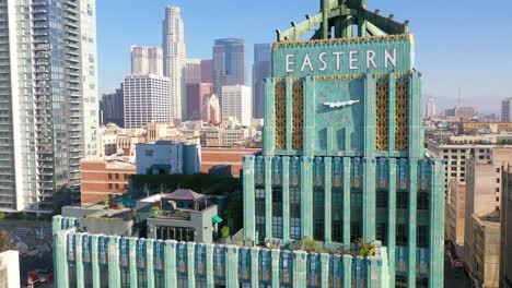 Aerial-Of-The-Historic-Eastern-Building-In-Downtown-Los-Angeles-With-Clock-And-Downtown-City-Skyline-Behind-1
