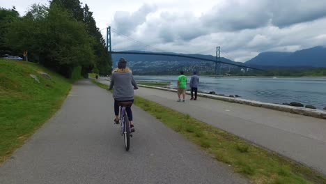 Eine-Fahrradkamera-Fängt-Die-Ansicht-Von-Hinten-Ein,-Während-Eine-Frau-Im-Stanley-Park-In-Vancouver-Mit-Dem-Fahrrad-Am-Ufer-Entlang-Fährt-1