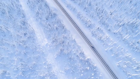Una-Vista-Aérea-Muestra-Un-Automóvil-Conduciendo-Por-Una-Autopista-Cubierta-De-Nieve-Arbolada-En-Suecia