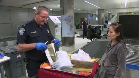 Passengers-Coming-Into-An-International-Airport-Terminal-Have-Bags-Inspected-By-Us-Customs